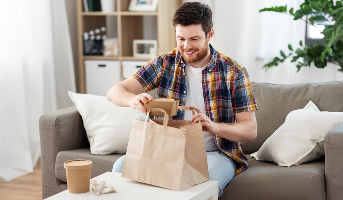A man sitting on his couch opening up his takeaway food bag