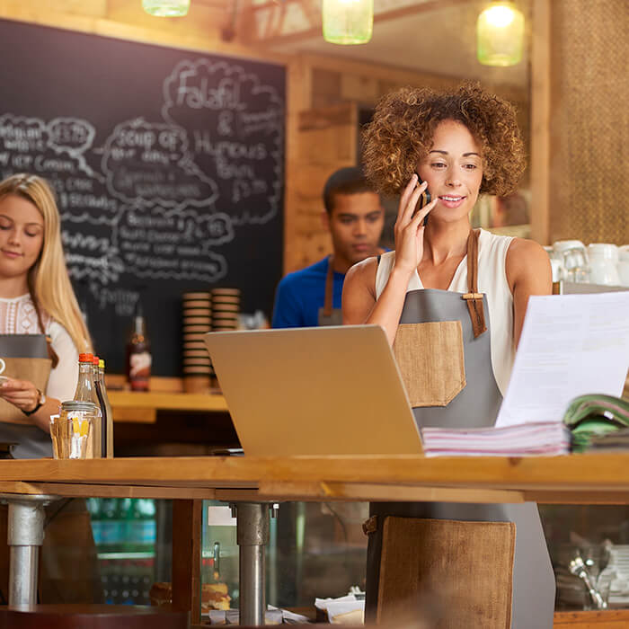 A business owner at her cafe on the phoen with staff working in the background.