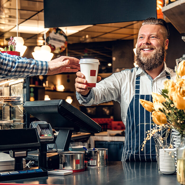 A Man handing a customer a coffee in front of the POS in a cafe