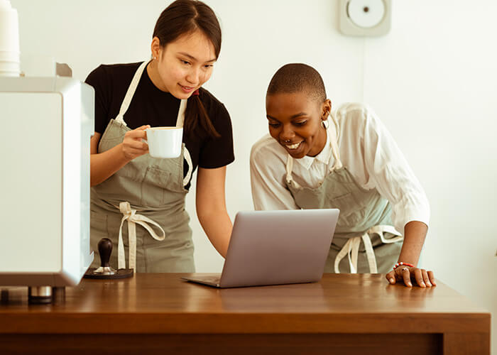 Two cafe workers looking at a laptop behind a counter.