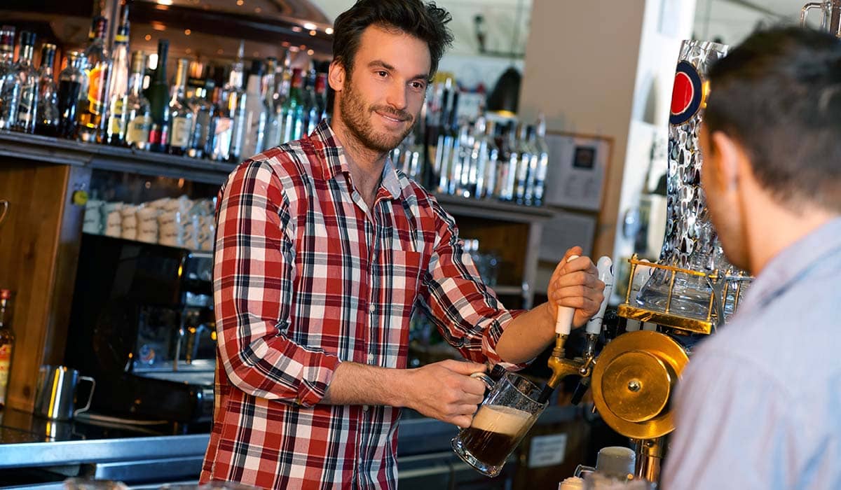 A bar person pouring a pint in a busy bar.
