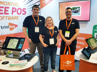 Triniteq team members smiling with POS equipment at a conference