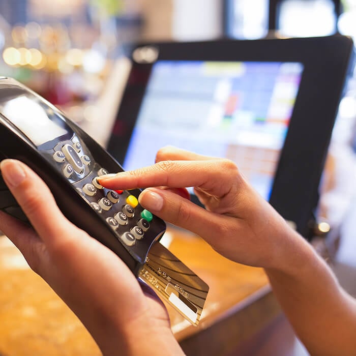 A close up of an EFTPOS machine being held with a POS touchscreen in the backgound